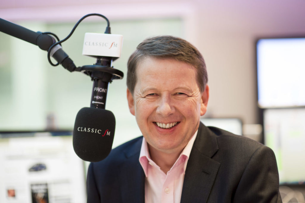 Bill Turnbull sits behind a radio microphone in the Classic FM studio. The room is brightly lit - Global